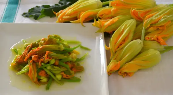 Fiori di zucca in padella, un piatto primaverile pronto da gustare. Accanto, fiori freschi in attesa di essere cucinati.