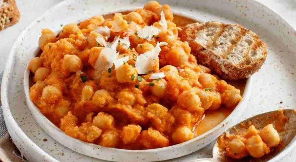 Minestra di ceci cremosa e saporita, guarnita con scaglie di parmigiano e accompagnata da pane tostato.