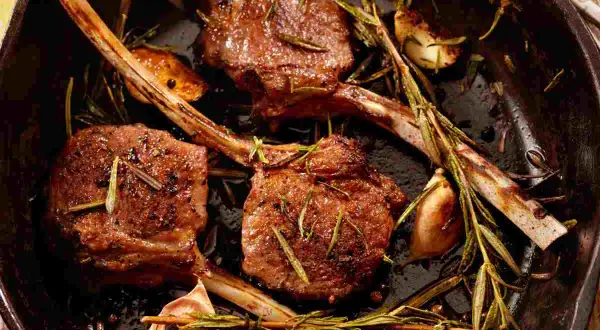 Tre succulenti costolette di agnello in padella, condite con rosmarino e aglio, pronte per essere gustate.