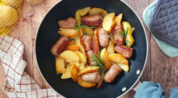 Salsiccia e patate in padella, dorate e profumate, con rametti di rosmarino. Un piatto rustico e invitante.