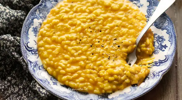 Un invitante risotto con la zucca cremoso, guarnito con pepe nero, su un piatto decorato con un motivo blu e bianco.