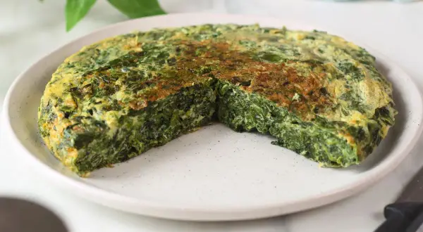 Frittata di spinaci dorata e soffice, tagliata a spicchi su un piatto bianco. Un piatto semplice e gustoso.