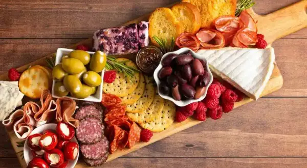 Un invitante tagliere salumi e formaggi con olive, lamponi, pane tostato e peperoncini ripieni.