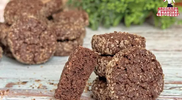 Biscotti al cioccolato rustici, ricoperti di zucchero grezzo, su un tavolo di legno. Uno spezzato rivela la consistenza friabile.