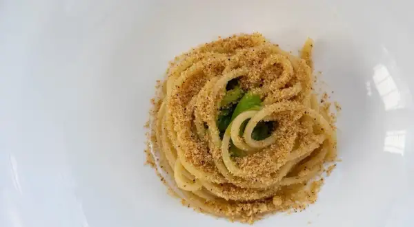 Un piatto di pasta alla carrettiera, spaghetti conditi con mollica tostata e verdure verdi, serviti su un piatto bianco.
