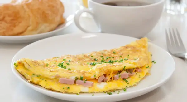 Deliziosa omelette con prosciutto e formaggio filante, guarnita con erba cipollina. Perfetta per una colazione o un brunch.