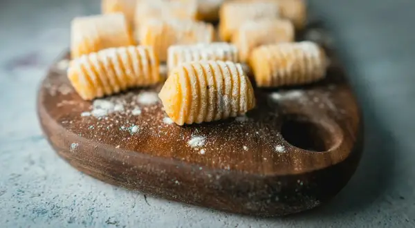 Gnocchi di patate ricetta originale pronti per essere cucinati, disposti su un tagliere di legno con un po' di farina sparsa.