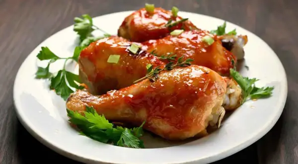 Tre cosce di pollo glassate, guarnite con erbe aromatiche e cipollotto, un delizioso pollo alla birra pronto da gustare.