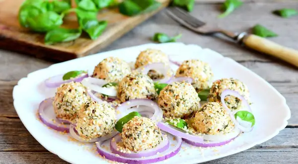 Deliziose polpette di ricotta impanate con semi di sesamo e erbe aromatiche, servite su un letto di cipolla rossa e foglie di basilico fresco.