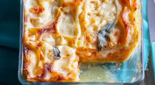 Lasagne con zucca dorate e filanti, guarnite con foglie di salvia, in una teglia di vetro.