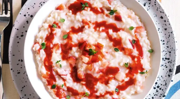 Un cremoso risotto alle fragole, guarnito con salsa di fragole e foglioline verdi.