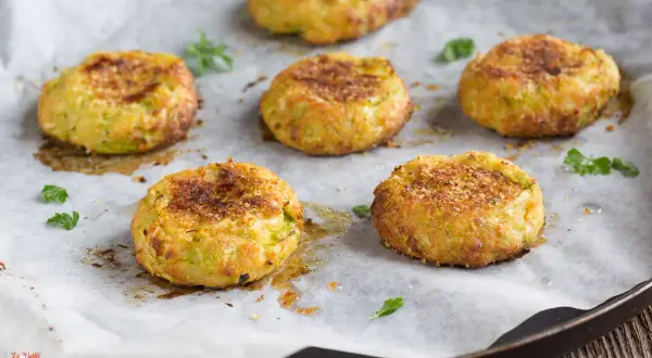 Sei polpette di zucchine dorate e croccanti, appena sfornate, su carta da forno.