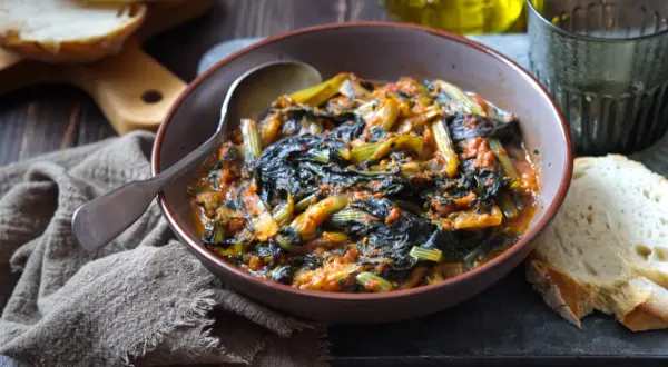 Cicoria in padella, un piatto rustico e saporito, servito in una ciotola con pane fresco e un bicchiere d'acqua.
