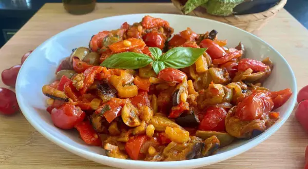 Caponata ricetta semplice: un piatto colorato con melanzane, peperoni, pomodorini e basilico fresco.