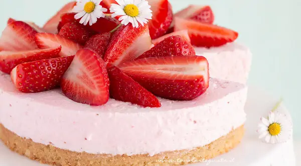Delizioso cheesecake alle fragole, decorato con fragole fresche e fiorellini bianchi.