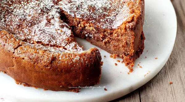 Una deliziosa torta al cioccolato al latte, cosparsa di zucchero a velo, con una fetta mancante che invita ad assaggiarla.