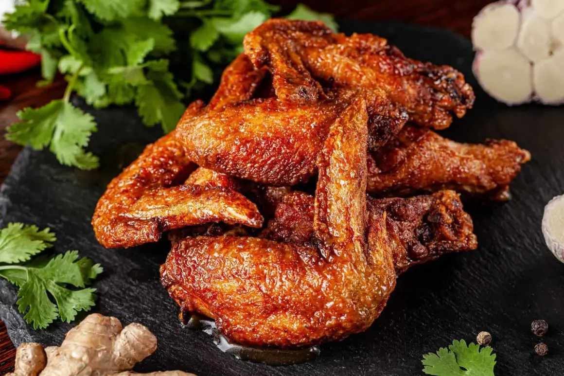 Alette di pollo al forno dorate e succulente, servite su una pietra scura con coriandolo fresco, zenzero e aglio.