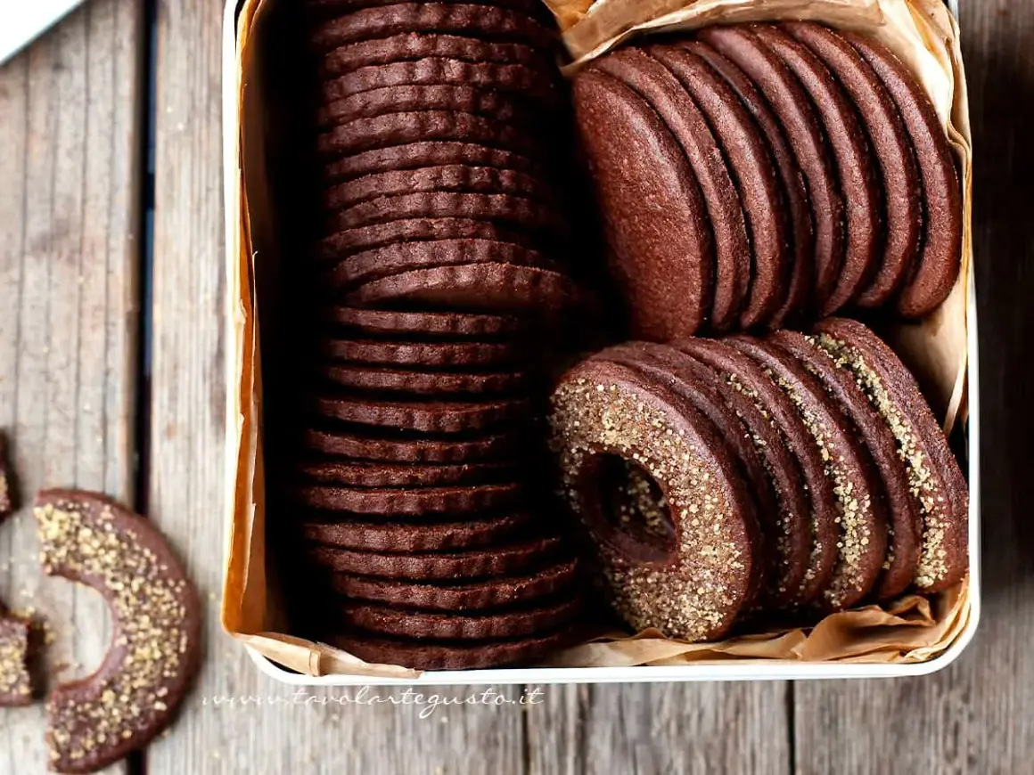 Una scatola piena di deliziosi biscotti al cacao, alcuni impilati in modo ordinato, altri con un bordo dorato croccante.