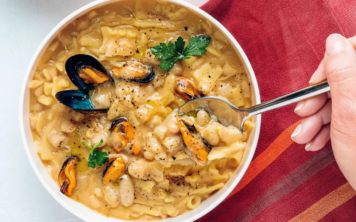 Un cucchiaio raccoglie una porzione di pasta fagioli e cozze, un piatto ricco e saporito, guarnito con prezzemolo fresco.