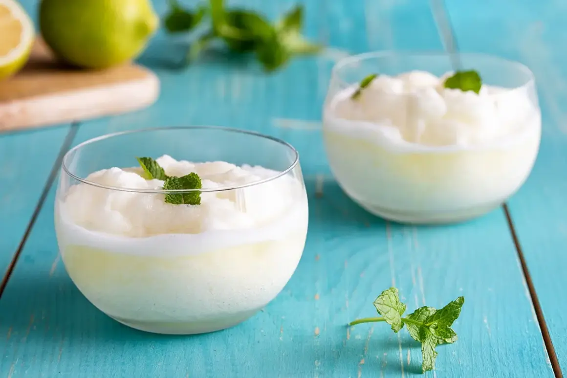 Due bicchieri di sorbetto al limone cremoso, guarniti con menta fresca, su un tavolo di legno blu.