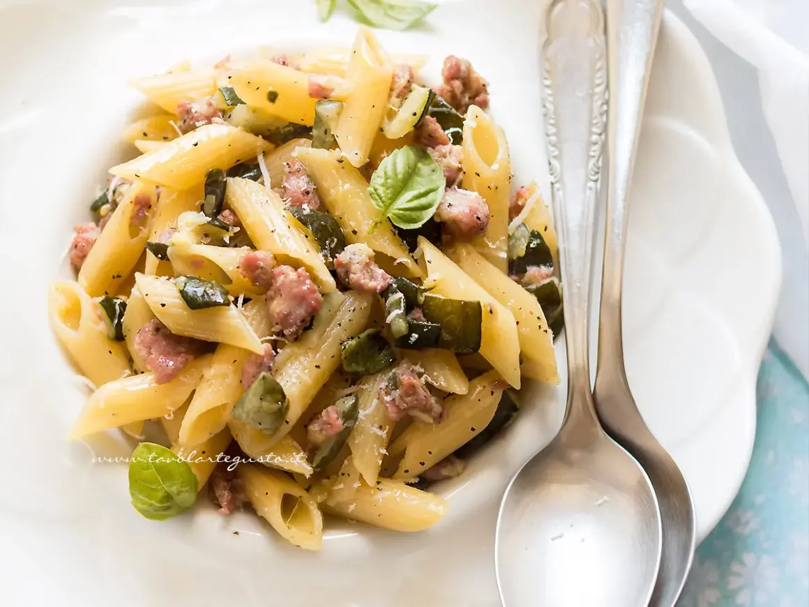 Penne con zucchine e salsiccia, un piatto gustoso e facile da preparare, guarnito con basilico fresco e parmigiano.