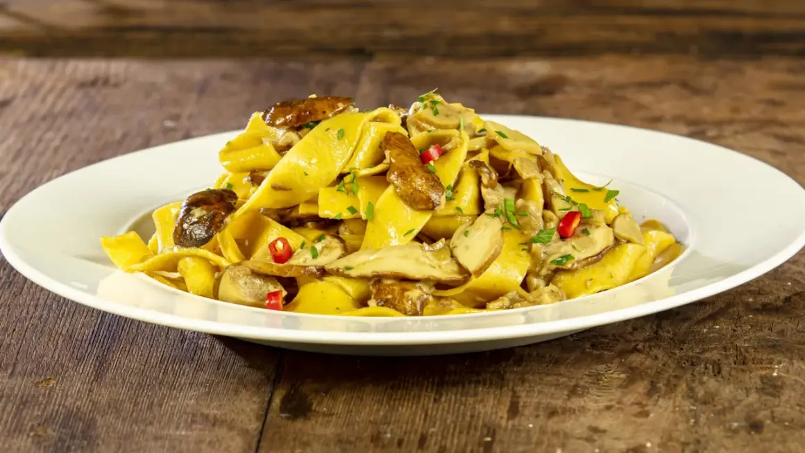 Un piatto invitante di tagliatelle ai funghi porcini, guarnite con peperoncino e prezzemolo fresco, su un tavolo di legno rustico.