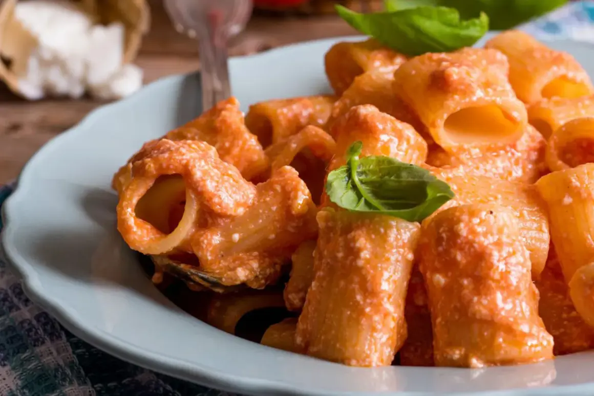Piatto di pasta con sugo cremoso di ricotta e pomodorini, guarnito con basilico fresco.