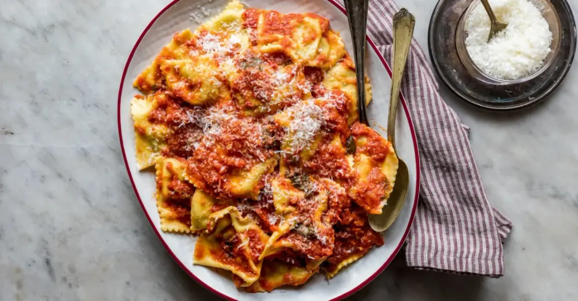 Piatto di tortelli di patate fatti in casa, conditi con sugo rosso e parmigiano grattugiato, pronti per essere gustati.