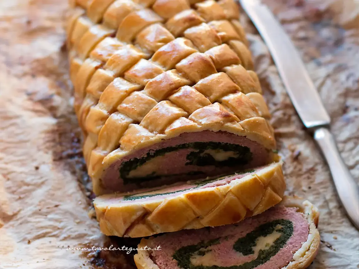 Un delizioso polpettone in crosta, con un ripieno di carne, spinaci e formaggio, pronto per essere affettato.