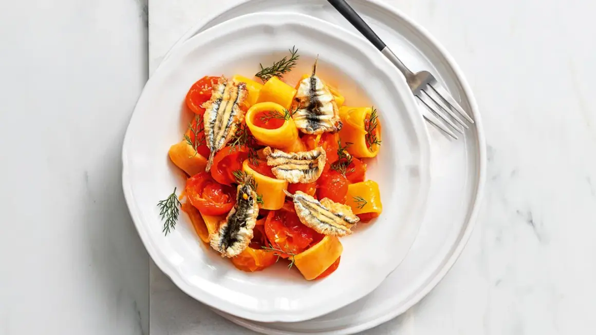 Piatto di pasta con pomodorini e croccanti alici fresche, guarnito con aneto.