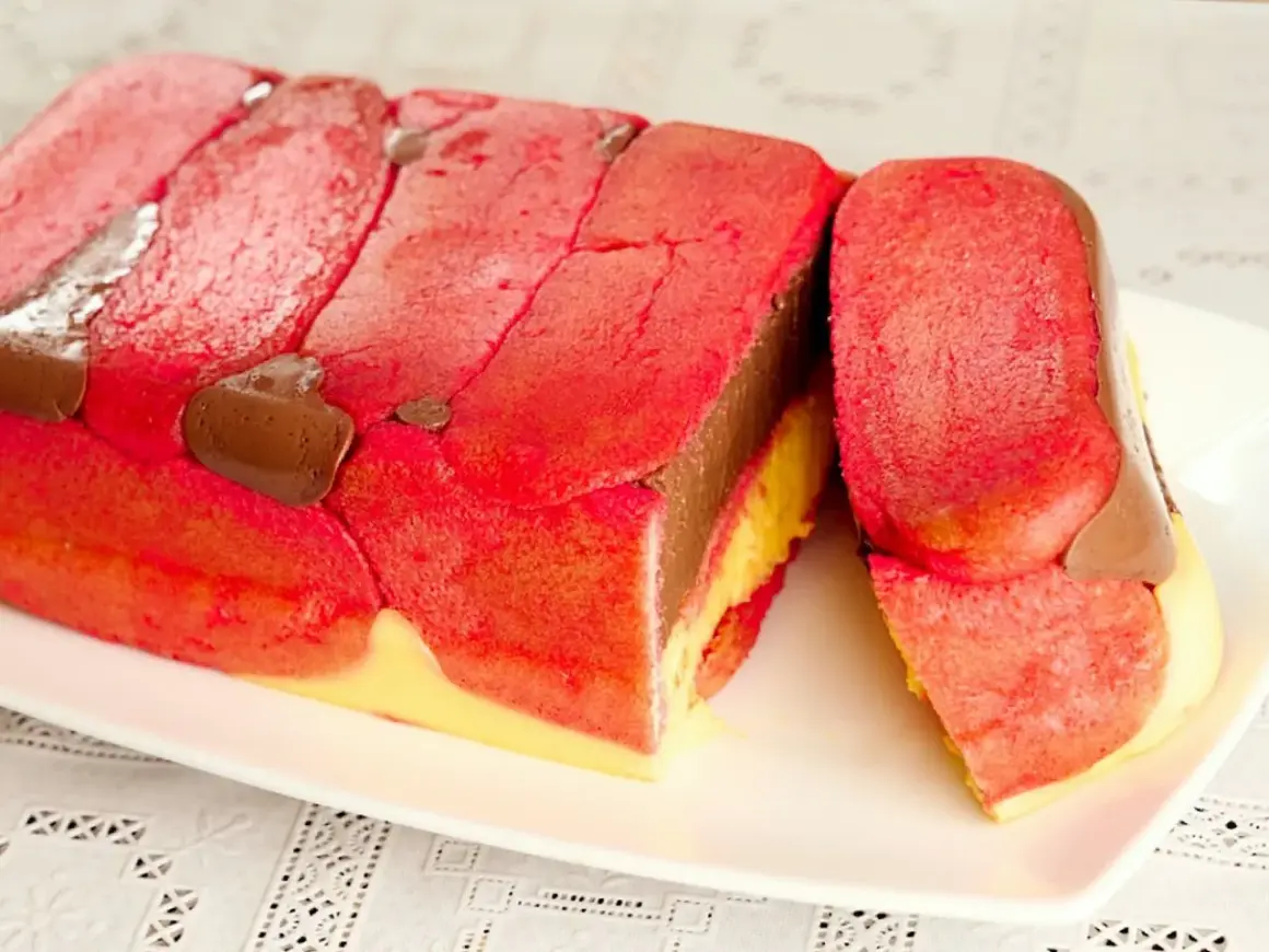 Una fetta di zuppa inglese tradizionale, con savoiardi rossi, crema al cioccolato e crema gialla.