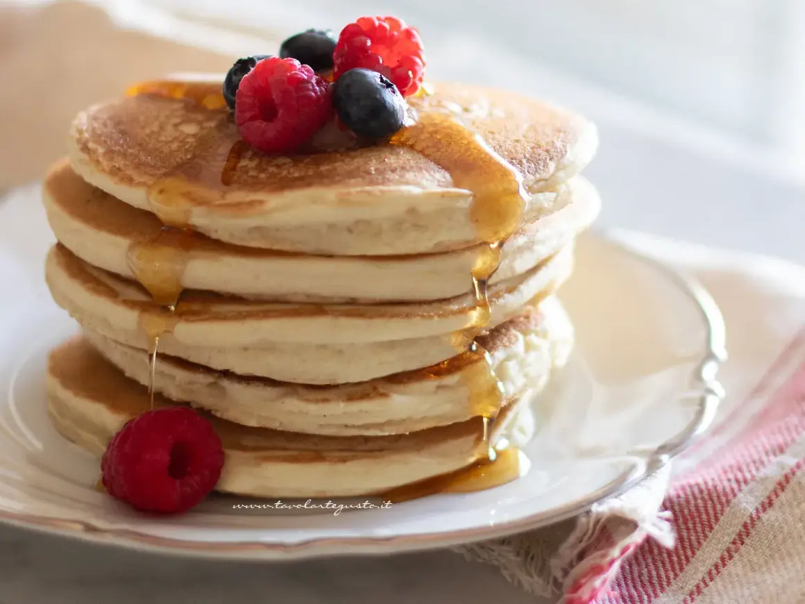Pancakes senza uova soffici e dorati, inzuppati di sciroppo d'acero e guarniti con frutti di bosco freschi.
