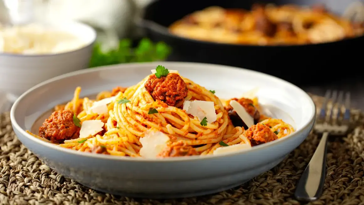 Un piatto invitante di spaghetti con ragù di salsiccia, guarnito con scaglie di parmigiano e prezzemolo fresco.