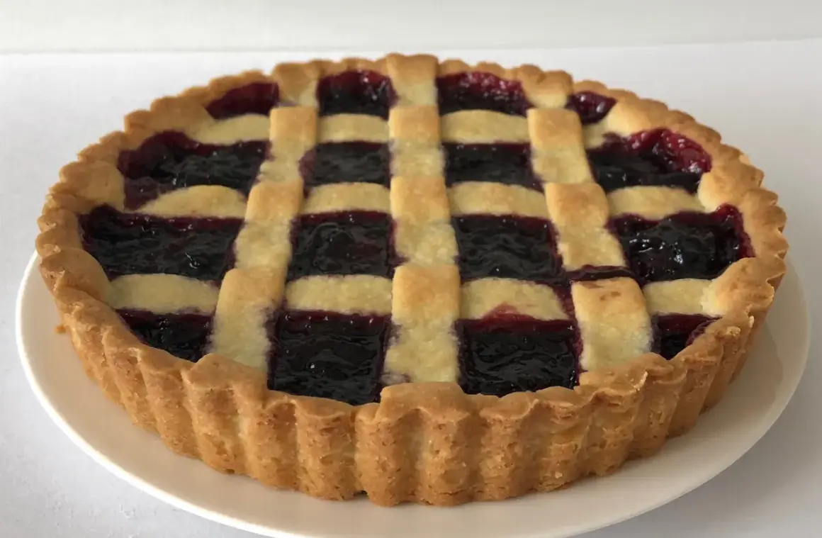 Una crostata di marmellata con una griglia di pasta dorata e un ripieno scuro e invitante.