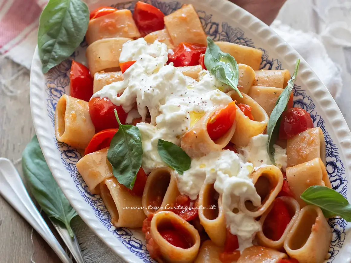 Piatto di pasta con pomodorini e burrata cremosa, guarnito con basilico fresco. Un'esplosione di sapori mediterranei.