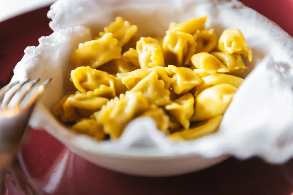 Un primo piatto invitante di ravioli del plin, piccoli e dorati, serviti in una ciotola bordata di bianco.