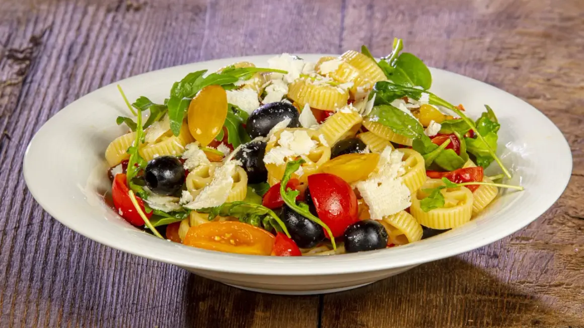 Pasta alla crudaiola con pomodorini, olive nere, rucola e scaglie di parmigiano. Fresca e colorata, un piatto estivo perfetto.