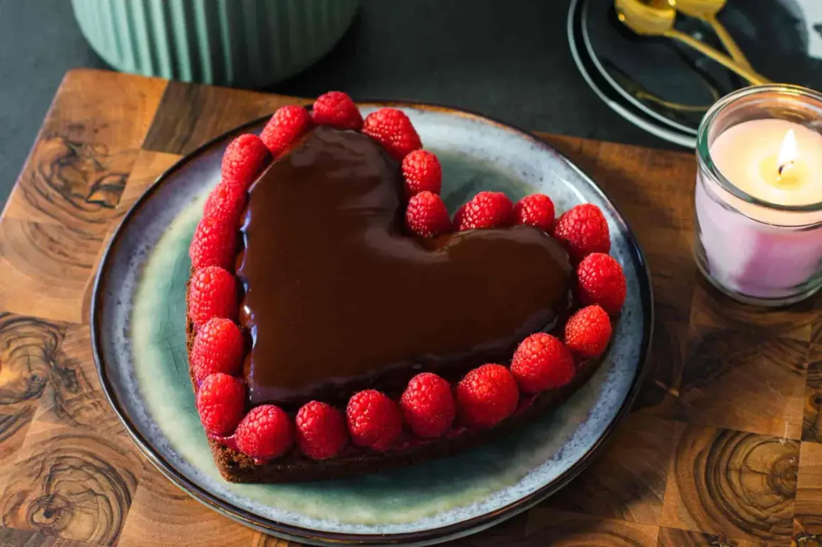 Deliziosa torta a forma di cuore ricoperta di cioccolato fuso e decorata con lamponi freschi, perfetta per un'occasione speciale.