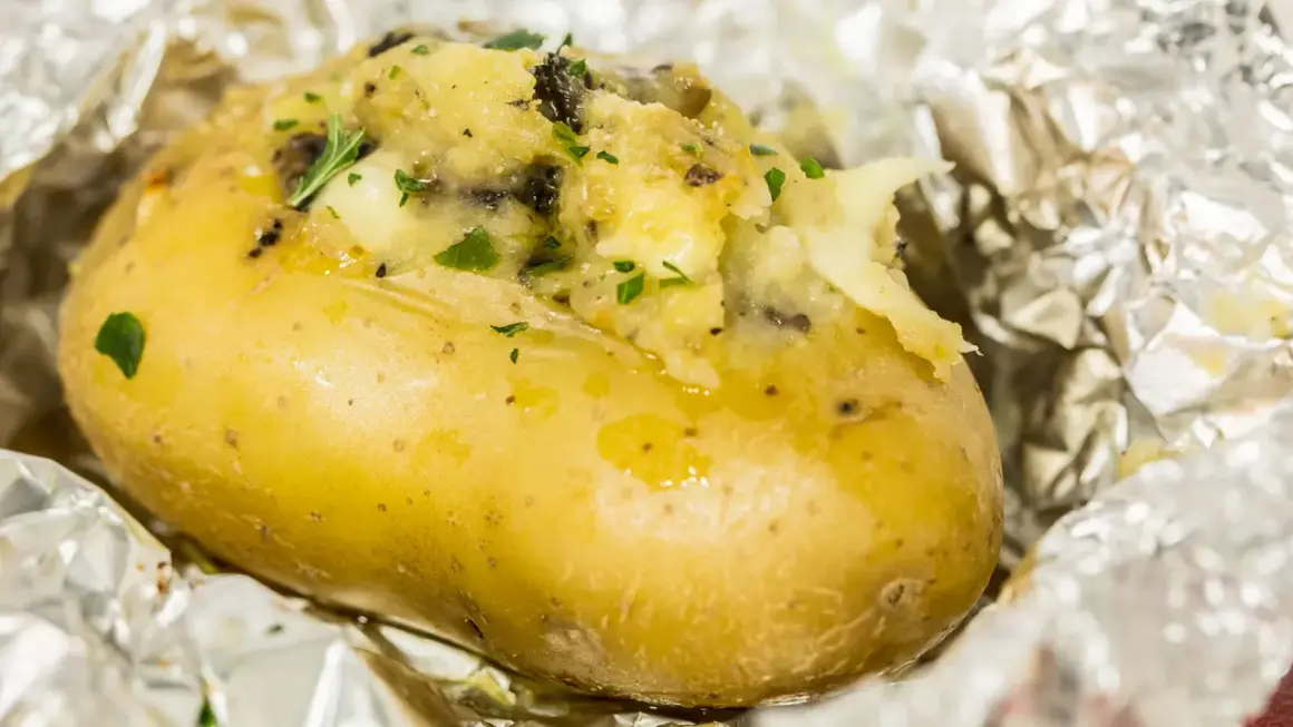 Patate ripiene al forno, dorate e fumanti, avvolte in carta stagnola, con un ripieno cremoso e erbe aromatiche.