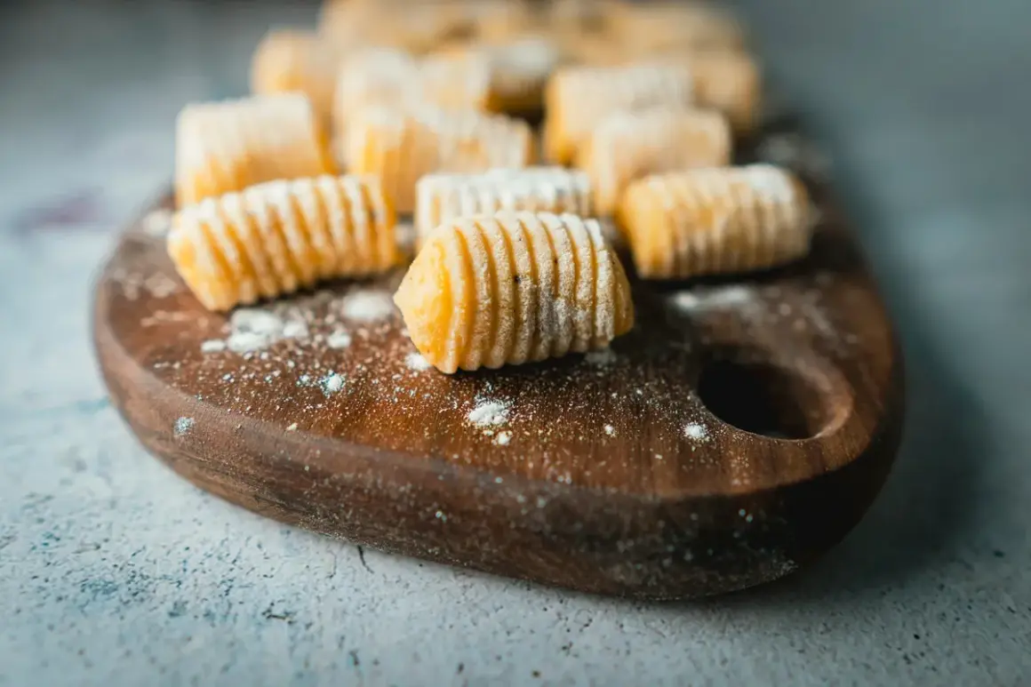 Gnocchi di patate ricetta originale pronti per essere cucinati, disposti su un tagliere di legno con un po' di farina sparsa.