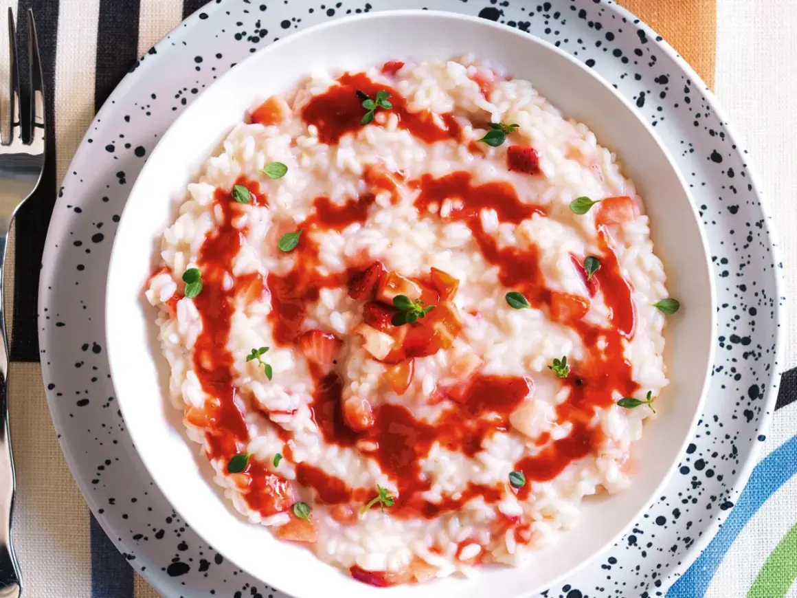Un cremoso risotto alle fragole, guarnito con salsa di fragole e foglioline verdi.