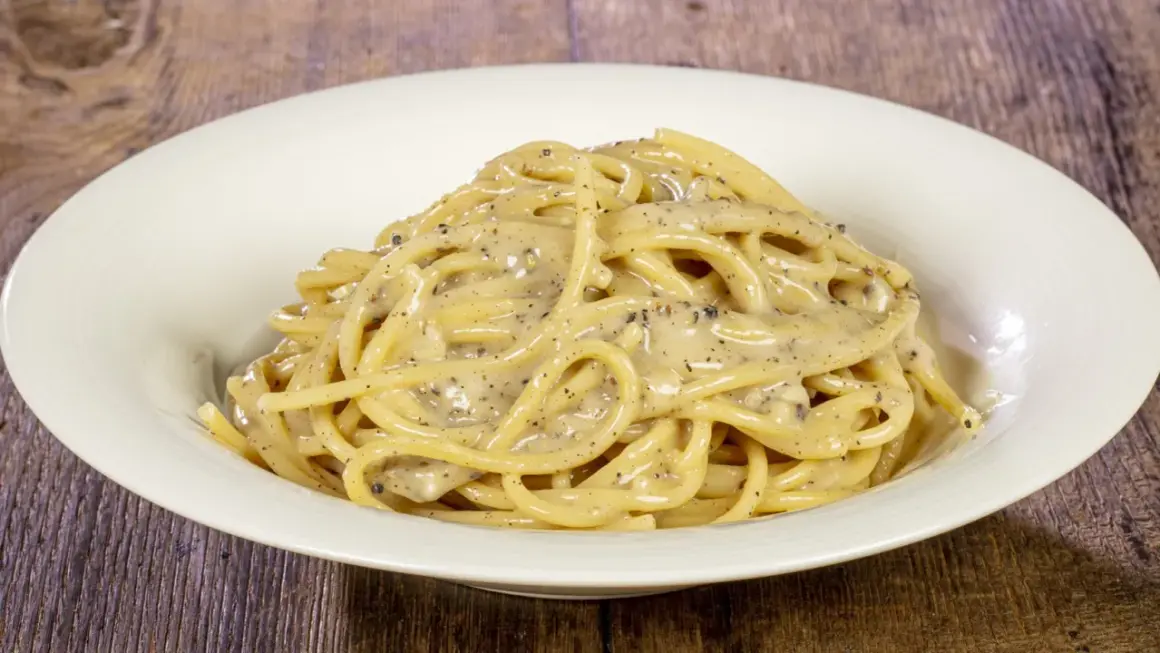 Un piatto di spaghetti cremosi, conditi con il classico cacio e pepe, con abbondante pepe nero macinato.