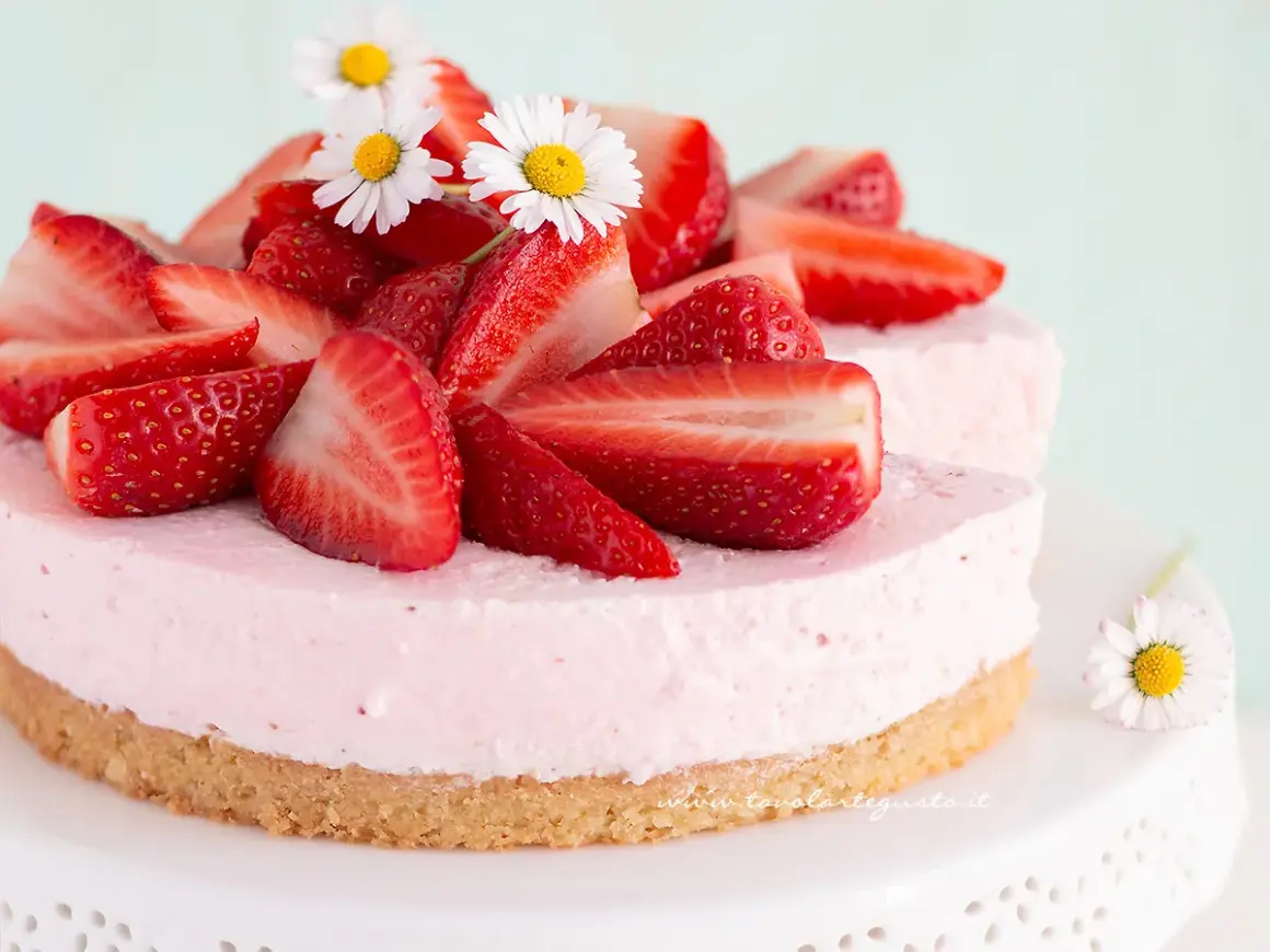 Delizioso cheesecake alle fragole, decorato con fragole fresche e fiorellini bianchi.