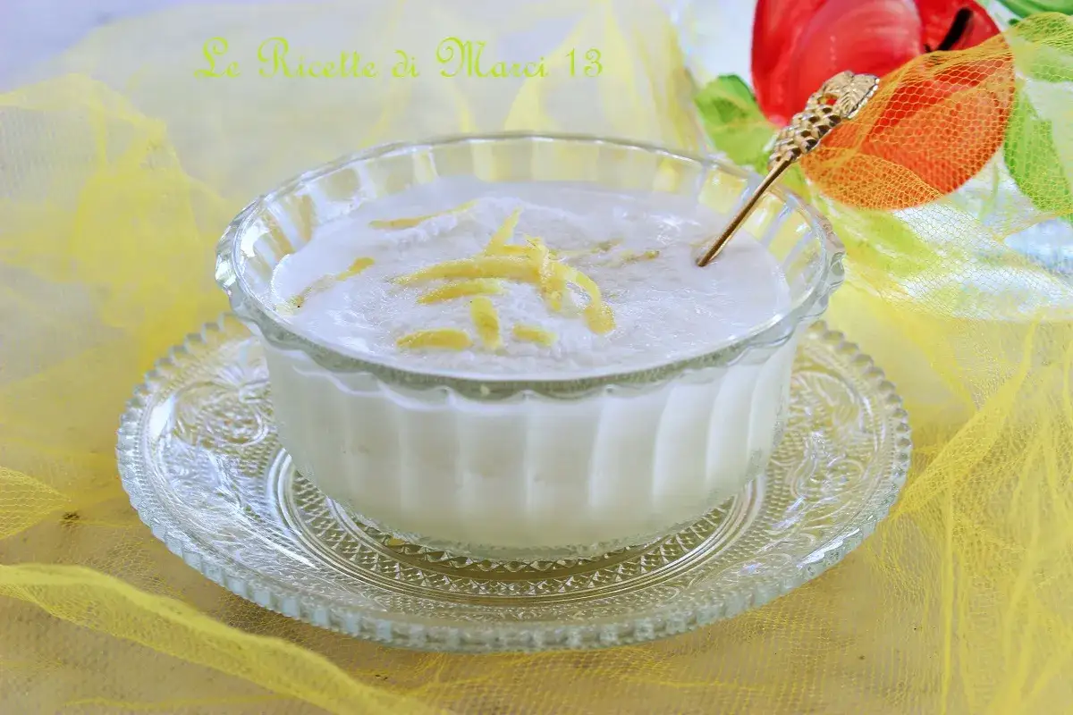 Un delizioso sorbetto al limone cremoso, guarnito con scorzette gialle, servito in una coppa di vetro su un piattino decorato, con un velo giallo sullo sfondo.
