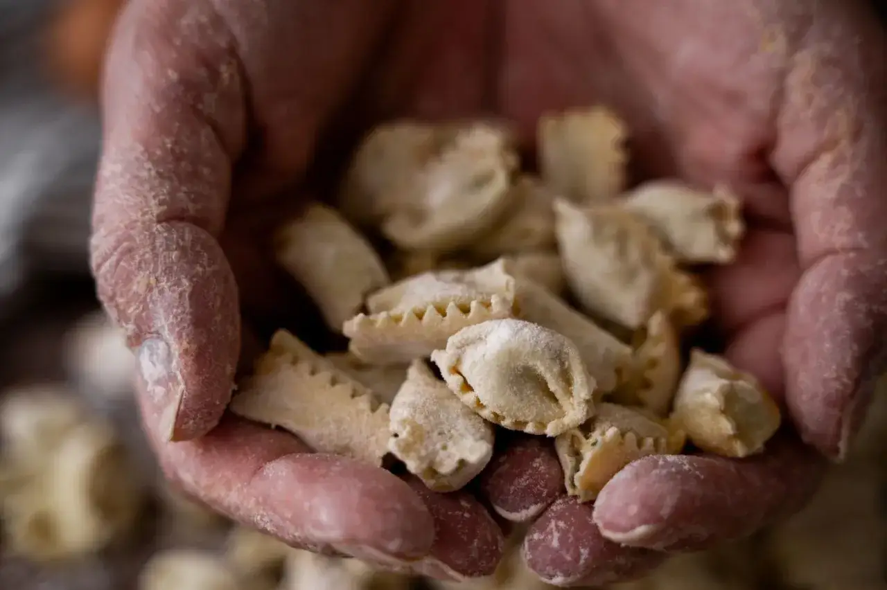 Mani infarinate tengono un mucchio di ravioli del plin, piccoli e fatti a mano, pronti per essere cucinati.