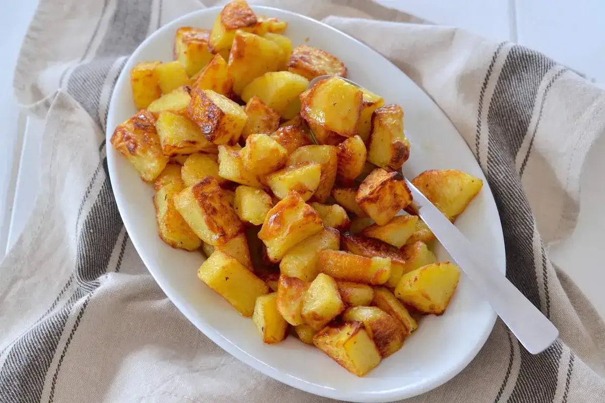 Un piatto bianco pieno di patate al forno dorate e croccanti, pronte per essere gustate.