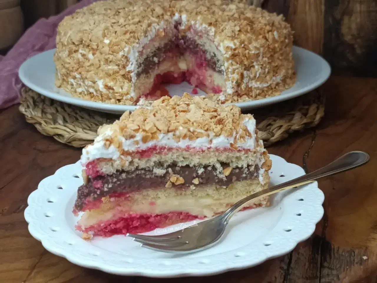 Una fetta di zuppa inglese tradizionale, con strati di pan di Spagna, crema pasticcera, cioccolato e fragole, ricoperta di panna e granella di nocciole.