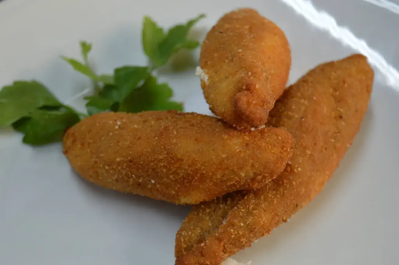 Fiori di zucca in pastella dorati e croccanti, serviti su un piatto bianco con un rametto di prezzemolo.