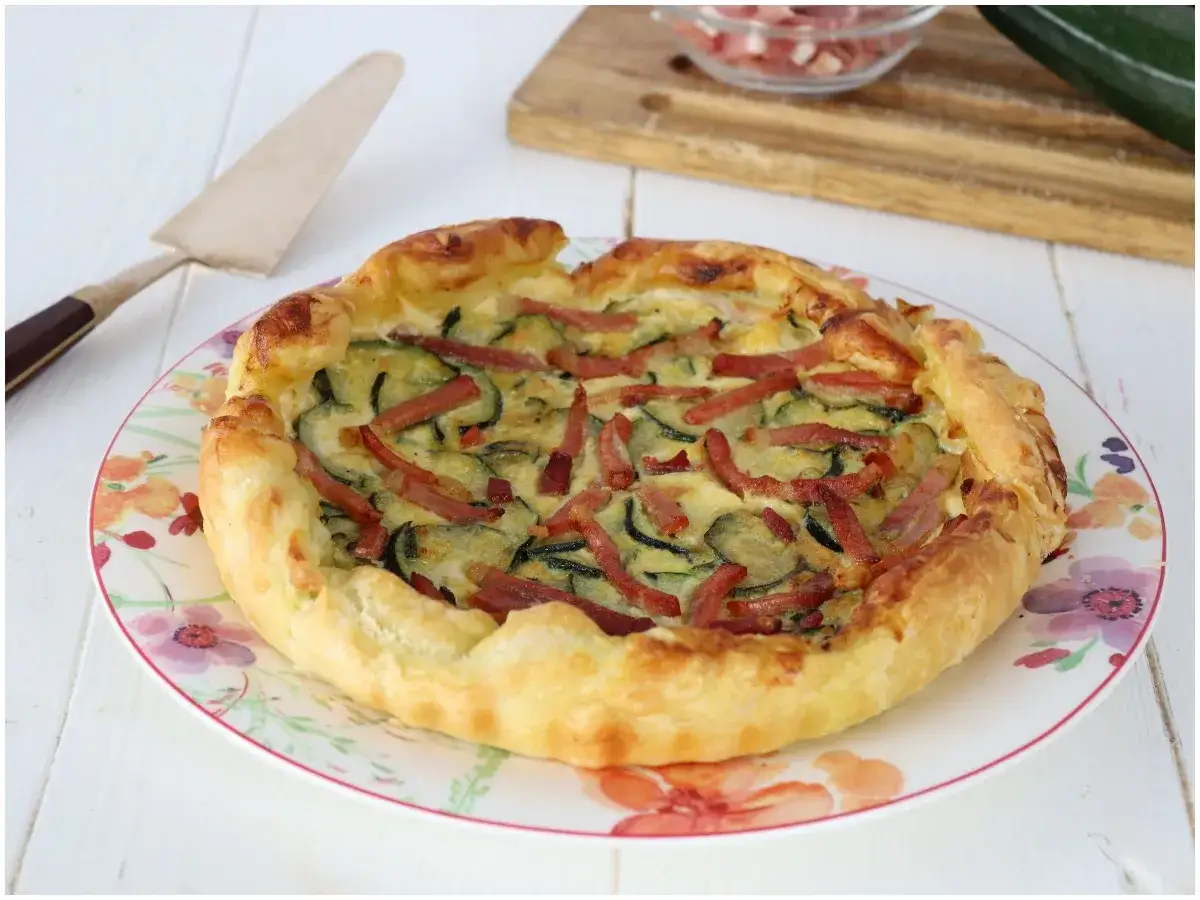 Torta salata zucchine e speck dorata e invitante, con un ripieno cremoso e striscioline di speck croccante.