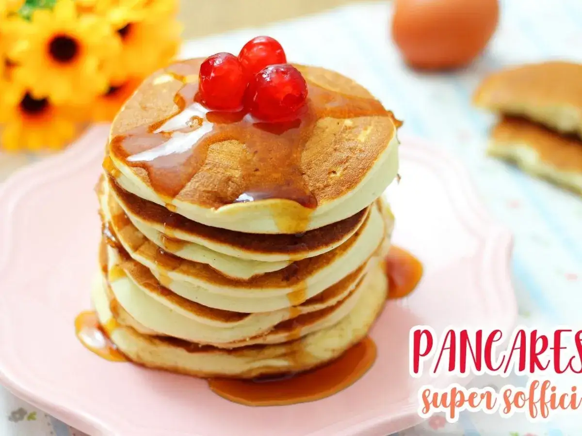 Pancakes senza uova, soffici e dorati, inzuppati nello sciroppo d'acero e guarniti con ciliegie rosse.